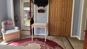 A room with a wooden door, a television mounted on the wall, a chair with a quilt, and a patterned rug. - Fernwood Guesthouse Garden Room, 1 of 2, near Dreams Park and Arnold Lake (Milford)