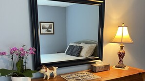 A wooden dresser with drawers, a mirror, a small table with a lamp, and a potted plant. - Fernwood Guesthouse Garden Room, 1 of 2, near Dreams Park and Arnold Lake (Milford)