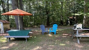 A picnic setup with a table, two Adirondack chairs, a green picnic table, and an orange umbrella. - Fernwood Guesthouse Garden Room, 1 of 2, near Dreams Park and Arnold Lake (Milford)