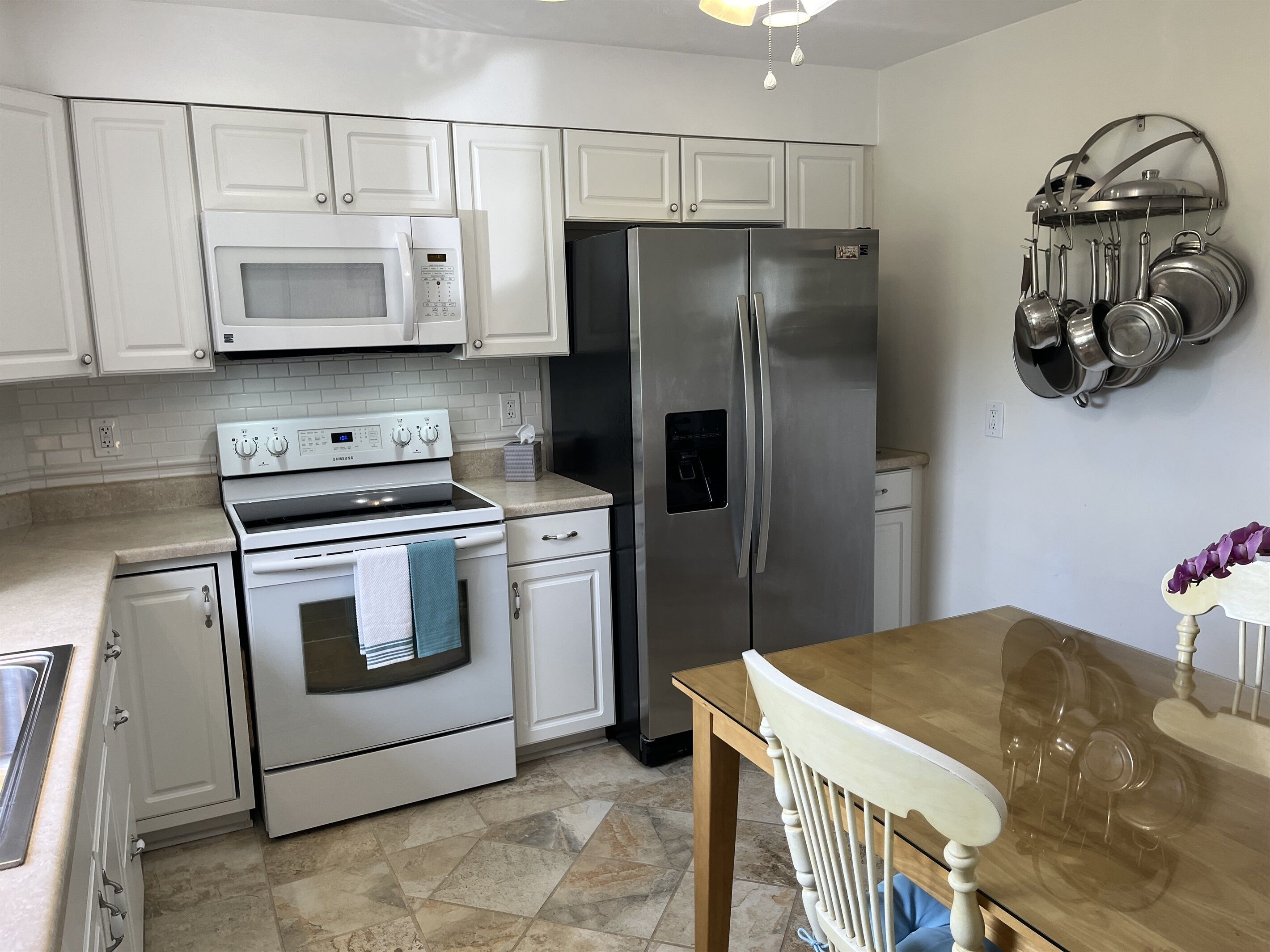 A kitchen with white cabinets, a stainless steel refrigerator, a microwave, an oven, and a dining table with chairs.