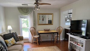 Sala de estar com sofá, duas cadeiras, mesa de jantar, televisão e área de cozinha com panelas e utensílios.