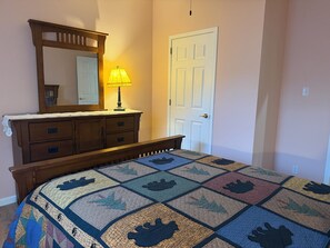 A bedroom with a wooden dresser, a mirror, a door, and a quilt with animal prints.