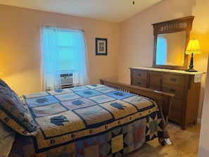 A bedroom with a bed, dresser, mirror, and window with blinds.