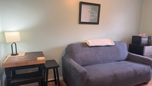 A room with a grey sofa, a small wooden table with a lamp, a framed picture on the wall, and a microwave on a cabinet. - Grandview Private 2 room suite, 5 minutes to Dreams Park, close to town (Milford)