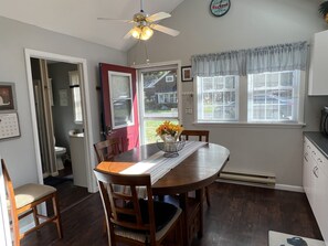 Un coin repas avec une table en bois, des chaises, un ventilateur de plafond et une fenêtre avec des stores.