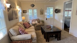 Een woonkamer met een bank, een salontafel en een lamp. Er is een deur die naar een andere kamer leidt.