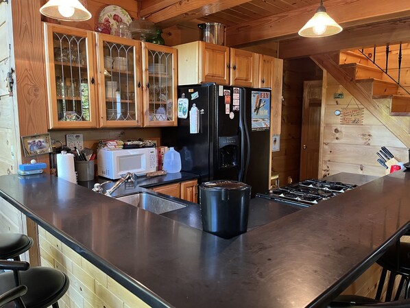A kitchen with wooden cabinets, a black refrigerator, a microwave, and a coffee maker. - Great Catch Cabin - Exquisite Log Cabin on Goodyear Lake w/ hot tub (Maryland)
