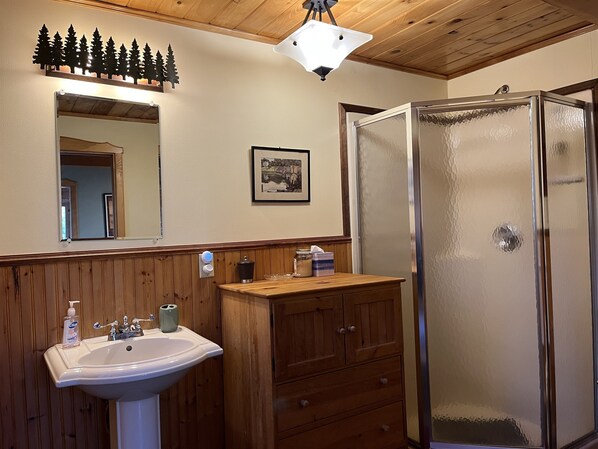 A bathroom with a wooden vanity, a sink, a mirror, a framed picture, and a frosted glass shower enclosure.