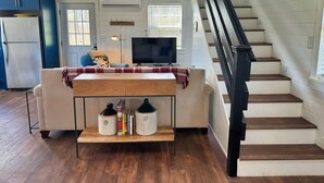 A modern living room with a sofa, a coffee table, a TV, and a staircase. - Grousehall Total Renovation, contemporary design, short drive to Cooperstown (Schuyler Lake)