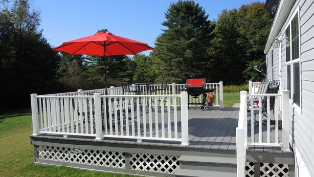 Une terrasse dotée d’une balustrade blanche, d’un parasol rouge et de mobilier d’extérieur.