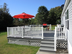 A deck with a white railing, a red umbrella, and outdoor furniture. - Groveside Quiet country setting, fire pit, ranch home w/ spacious rear deck (Maryland)