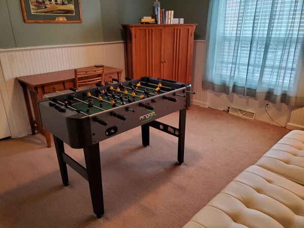 A room with a foosball table, a wooden cabinet, and a window with curtains. - Groveside Quiet country setting, fire pit, ranch home w/ spacious rear deck (Maryland)