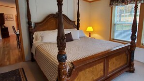 Un lit à baldaquin avec une structure en bois et une tête de lit, une table de chevet avec une lampe, et une fenêtre avec des stores.