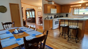 Un coin repas avec une table en bois dressée pour quatre personnes, une cuisine équipée d’un four à micro-ondes et d’une cuisinière, et un bar avec des tabourets.