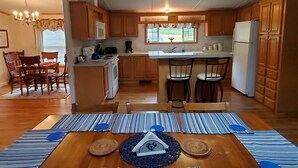 Une cuisine compacte avec des meubles en bois, un îlot central, une table à manger avec des sets de table à rayures et un lustre.
