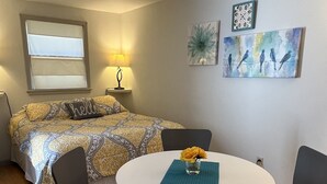 Habitación de hotel con cama, una mesa redonda con sillas, un florero con flores y obras de arte en la pared.