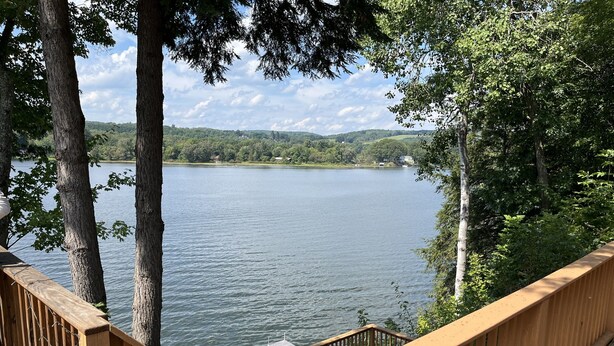 A wooden deck overlooking a calm lake with trees and distant hills.