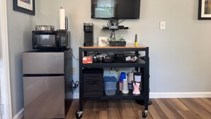 A kitchenette with a refrigerator, microwave, coffee maker, and a TV on a wall-mounted stand.