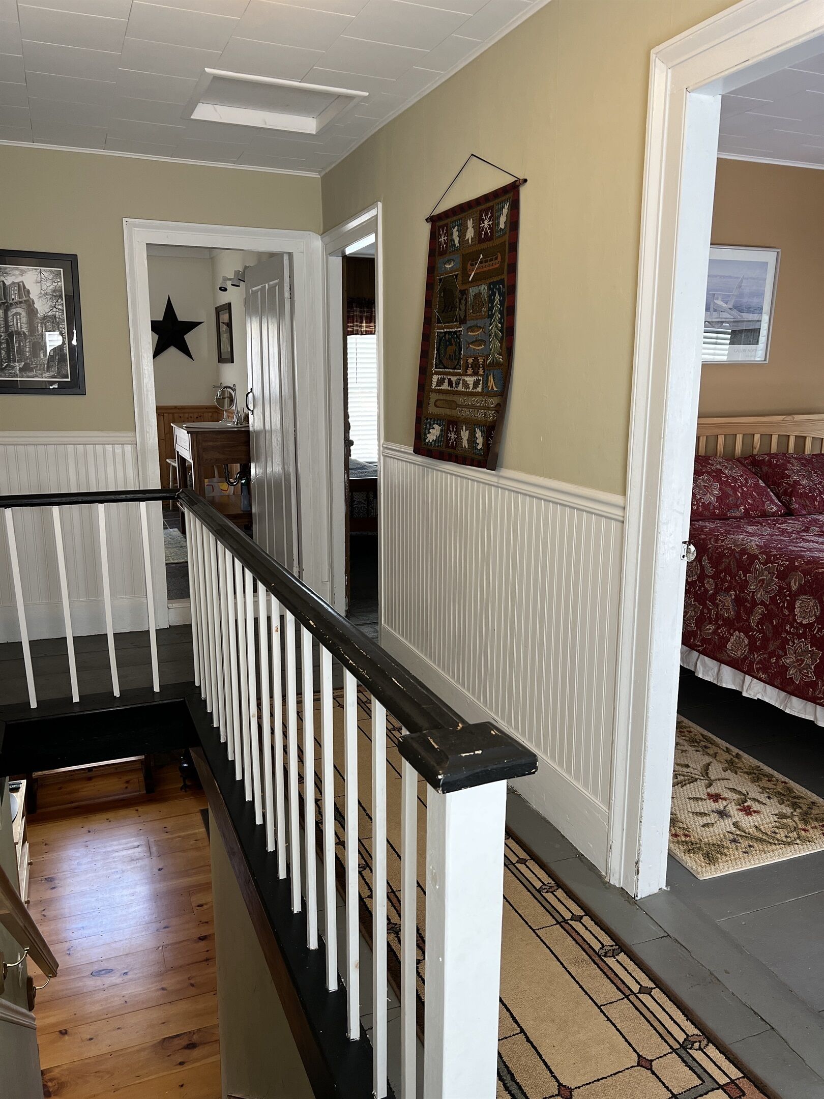 A staircase with white railings leading to a bedroom with a red floral bedspread.