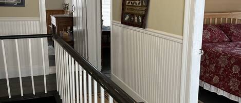 A staircase with white railings leading to a bedroom with a red floral bedspread.