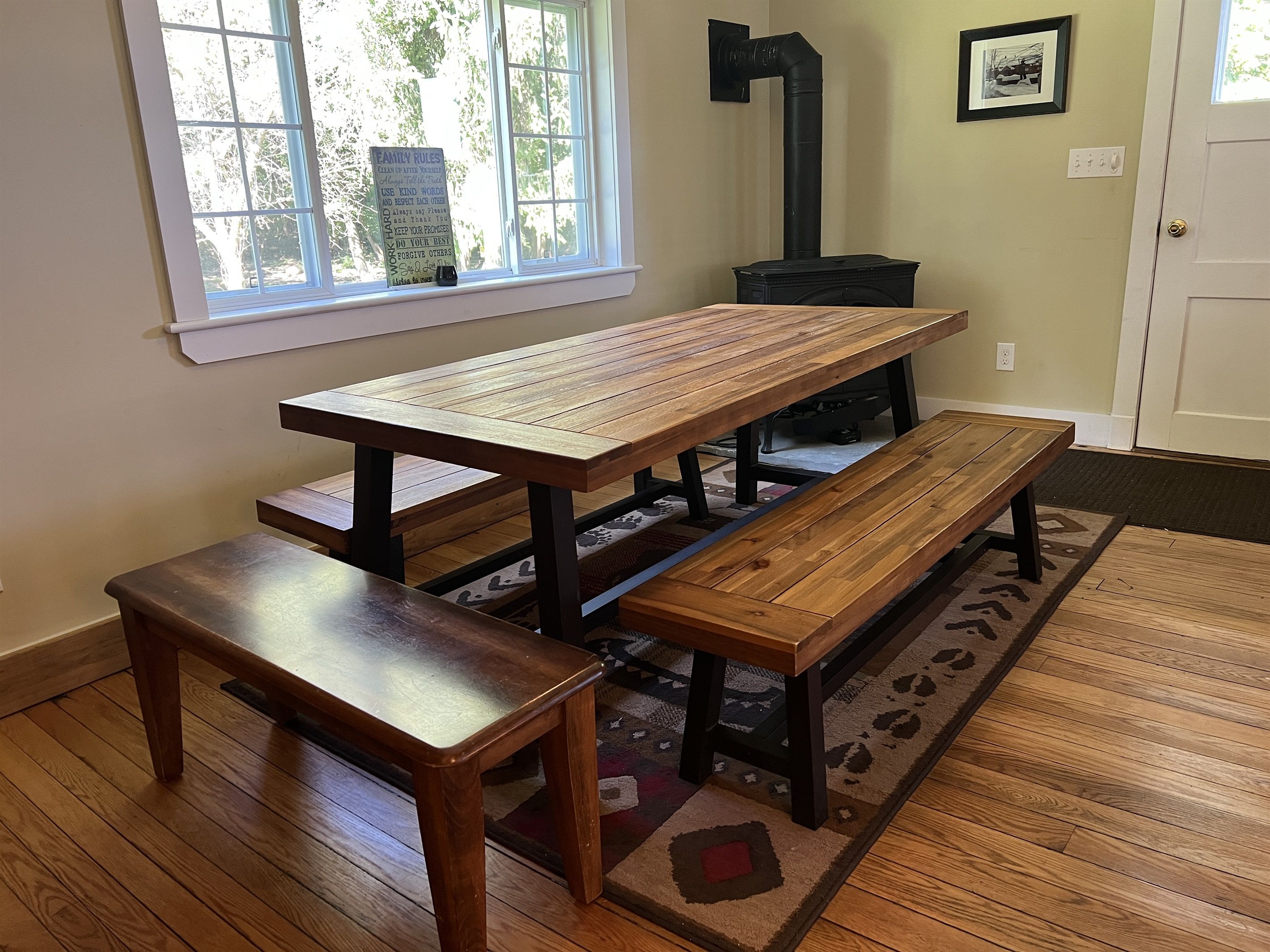 A wooden table with benches in a room with a window and a black stove.