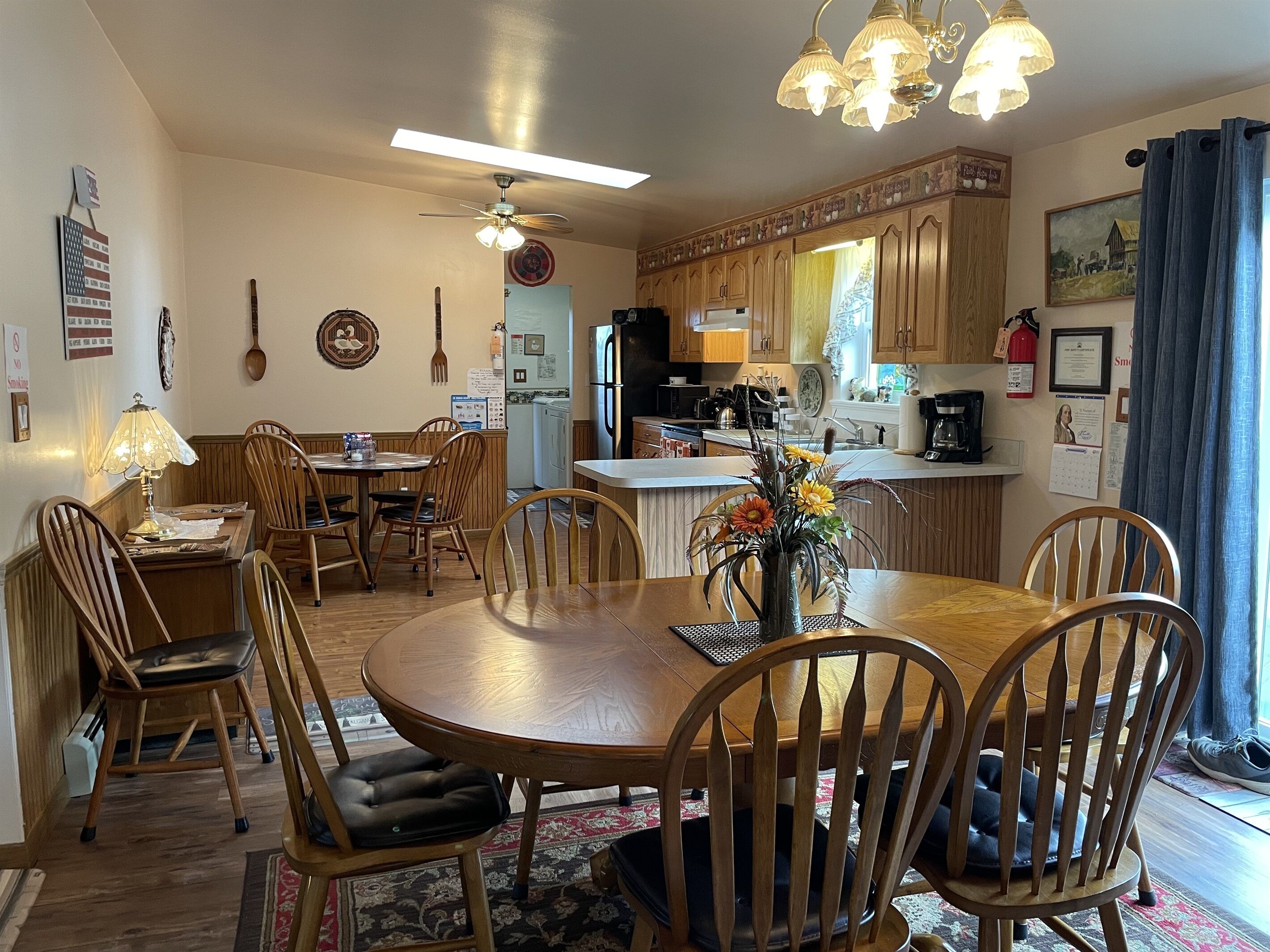 A dining area with a wooden table and chairs, a ceiling fan, and a kitchen in the background.
