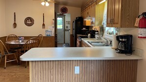 A kitchen with wooden cabinets, a dining area with a table and chairs, a ceiling fan, and a coffee maker. - Morgan Farm - Well cared for Ranch house near Canadarago Lake (Richfield Springs)