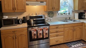 A kitchen with wooden cabinets, a microwave, a stove, a sink, and a window with a view of a house. - Morgan Farm - Well cared for Ranch house near Canadarago Lake (Richfield Springs)