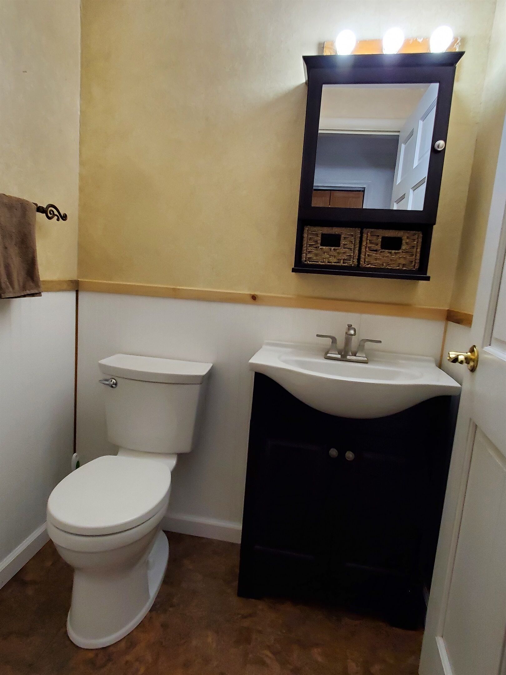 Une salle de bain avec des toilettes blanches, un meuble-lavabo noir et un miroir au-dessus du meuble-lavabo.