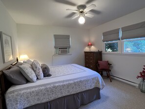 Un dormitorio con cama, ventilador de techo, cómoda, silla y ventana con persianas.