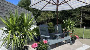 Een terras met een houten tafel en twee stoelen, omringd door potplanten en een gestreepte parasol.