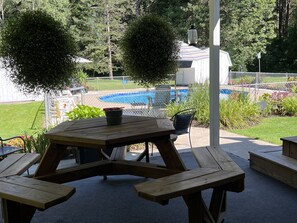Una mesa de picnic de madera con un cubo, rodeada de un jardín vallado y una piscina al fondo.