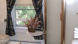 A bathroom with a shower, toilet, and a small table with a potted plant.