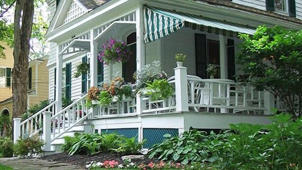 A two-story white house with a porch, stone pathway, and lush greenery.