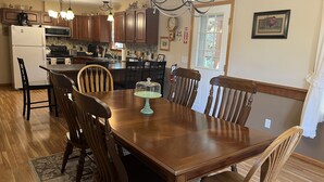 A dining area with a wooden table and chairs, a chandelier, and kitchen cabinets in the background. - Pagey's Place - Peaceful country setting, fire pit, Foosball, amazing views (Cooperstown)