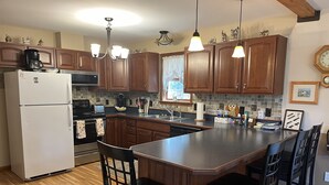 A kitchen with wooden cabinets, a white refrigerator, a built-in island with bar stools, and pendant lighting. - Pagey's Place - Peaceful country setting, fire pit, Foosball, amazing views (Cooperstown)