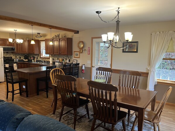 A modern kitchen with wooden cabinets, a central island, and pendant lighting. There is a dining area with a wooden table and chairs. - Pagey's Place - Peaceful country setting, fire pit, Foosball, amazing views (Cooperstown)