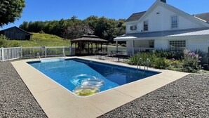 Ein rechteckiger Pool mit einer Laube und Sitzgelegenheiten im Freien, umgeben von einem weißen Zaun und Kies.