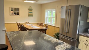Eine Küche mit einer großzügigen Marmorarbeitsplatte, Holzschränken, einem Edelstahlkühlschrank und einem Fenster mit Blick auf Grünflächen.