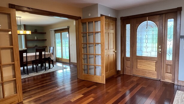 A spacious room with hardwood flooring, a dining area with a table and chairs, and a large wooden door with glass panels. - Phoenix Hill - Spacious, 7bdrm home, pool, game room and long distance views (West Oneonta)