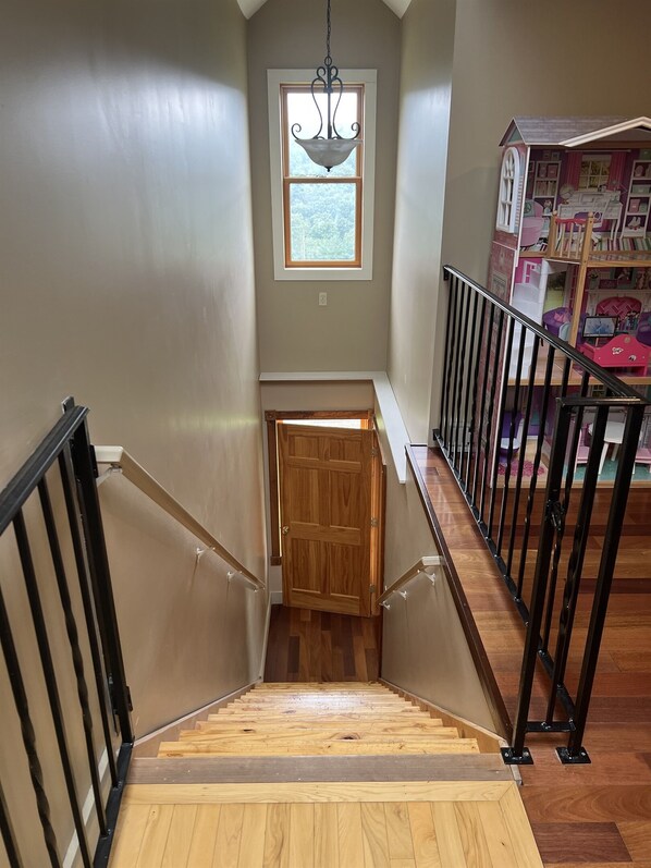 Un escalier en bois avec des rampes noires, une porte en bois en bas et une fenêtre au-dessus.