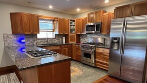 A modern kitchen with wooden cabinets, stainless steel appliances, and a granite countertop. - Phoenix Hill - Spacious, 7bdrm home, pool, game room and long distance views (West Oneonta)