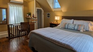 A bedroom with a large bed, a desk, and a chair. There is a window with blinds, a ceiling fan, and a lamp on the nightstand. - Pioneer Cottage Pristine 1 bedroom home, 5 minutes to All Star, private patio (Oneonta)