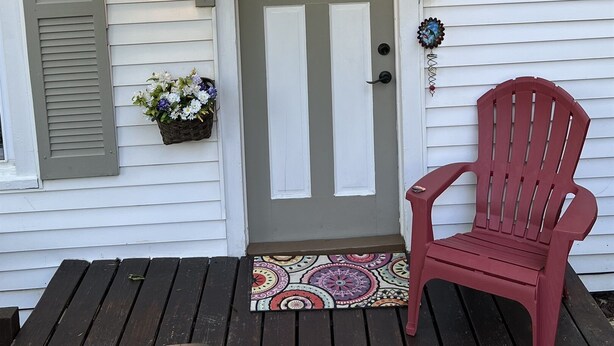 A house with a gray door, a mailbox, and a red chair on the porch. - Pioneer Cottage Pristine 1 bedroom home, 5 minutes to All Star, private patio (Oneonta)