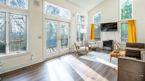 A spacious living room with large windows, a ceiling fan, and a flat-screen TV. - Updated Flooring, New Hot Tub, Resort Amenities! (Mc Gaheysville)