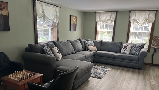 Sala de estar com sofá modular, uma poltrona preta, um tabuleiro de xadrez e um tapete.