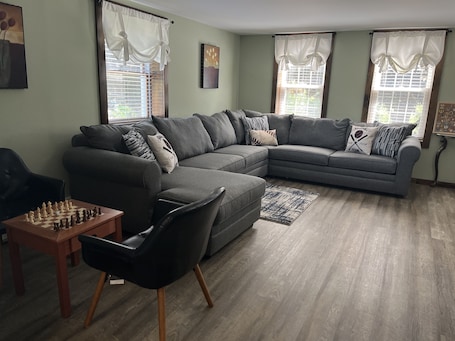 A living room with a sectional sofa, a black chair, a chessboard, and a rug.