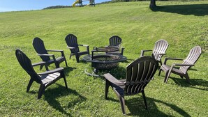 Uma área externa com gramado, cadeiras Adirondack e uma mesa de metal.