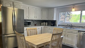 Uma cozinha moderna com armários brancos, eletrodomésticos de aço inoxidável e uma mesa de jantar de madeira com cadeiras.