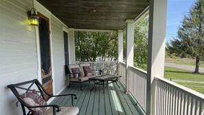 A porch with a green wooden floor, white railings, and two chairs with cushions.